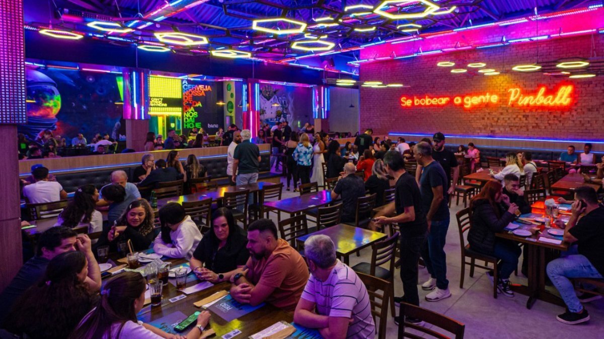Além dos jogos, o Bario Bar conta com um menu diversificado que inclui porções, lanches e o famoso Bario Burger. Há opções para todos os gostos, desde aperitivos veganos até sanduíches clássicos, como o Pac Man Burger, de linguiça toscana e cebola caramelizada. Foto: Divulgação/Instagram