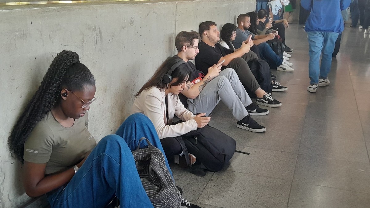 Passageiros estão sentados no chão da estação enquanto aguardam a normalização do trem. Divulgação/Guilherme Chagas