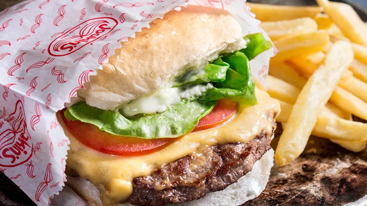 Com mais de 50 anos de história, o Joakin's Hamburguer mantém um dos ambientes mais icônicos da cidade: sofás vermelhos, salão amplo e clima descontraído. O cheese salada (R$ 43,70) é a estrela do cardápio, feito com disco de carne de 120g, queijo, alface, tomate verde e a famosa maionese verde. Foto: Reprodução/Divulgação