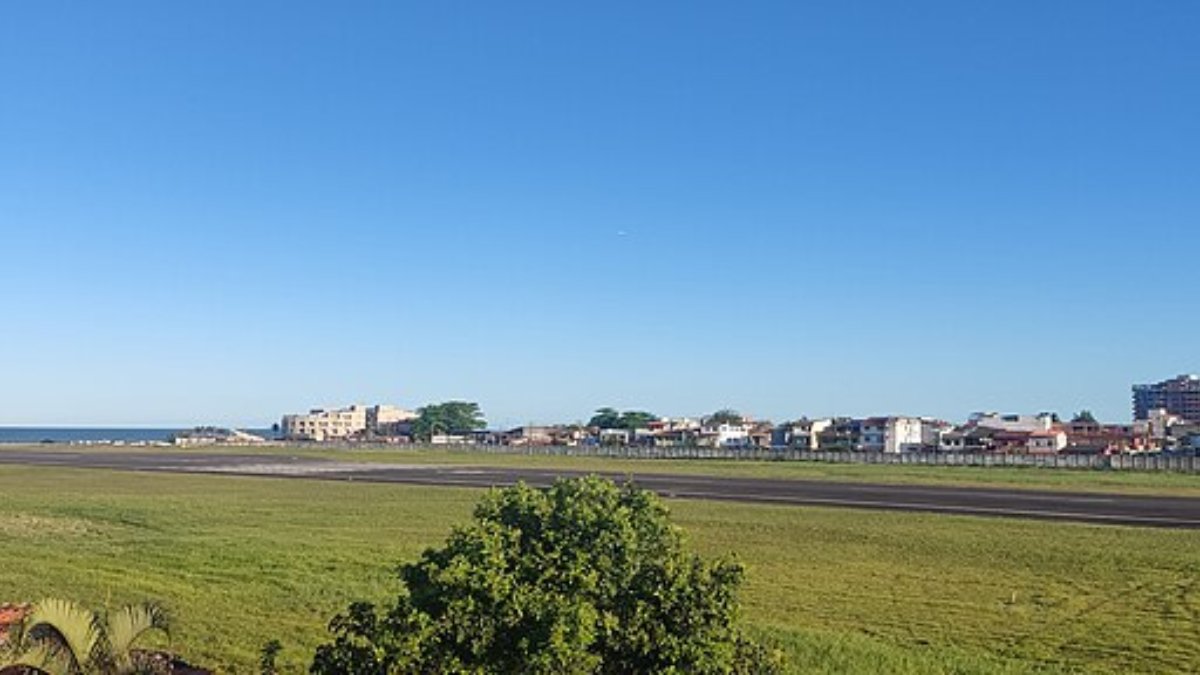 Localizado em uma das regiões mais turísticas da Bahia, o Aeroporto Jorge Amado, em Ilhéus, é um dos aeroportos mais desafiadores do Brasil. O que torna o aeroporto peculiar e arriscado é sua proximidade com o mar e a geografia que cerca a cidade. O Aeroporto Jorge Amado possui uma pista localizada bem próxima à orla, o que oferece aos passageiros uma vista incrível do oceano, mas ao mesmo tempo desafia os pilotos. Ventos fortes vindos do mar podem desestabilizar as aeronaves durante as manobras de pouso e decolagem. Outro ponto que agrava a complexidade deste aeroporto é o clima da região, que frequentemente alterna entre sol intenso e chuvas repentinas. Em dias nublados, a visibilidade reduzida se torna um fator de risco adicional, dificultando a precisão nas manobras de aterrissagem. Além disso, a pista relativamente curta em comparação a outros grandes aeroportos impõe restrições às aeronaves maiores, aumentando ainda mais o desafio para os pilotos, que precisam ser extremamente precisos em suas abordagens. Fotos: Wikimedia Commons