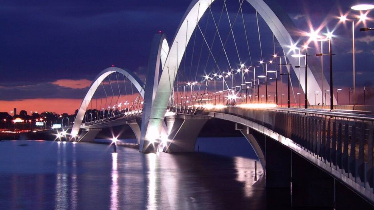 A beleza da Ponte JK vai muito além do concreto e do aço. O projeto assinado pelo arquiteto Alexandre Chan e pelo engenheiro Mário Vila Verde foi desenhado para reproduzir a leveza de uma pedra quicando sobre o espelho d'água. Essa simetria quebrada e a fluidez dos arcos estaiados garantiram ao monumento um lugar na prestigiada lista da Condé Nast Traveler. Estudos de arquitetura apontam que essa sensação de movimento é justamente o que torna a estética da ponte tão única e capaz de cativar observadores ao redor do mundo.