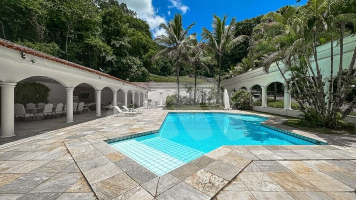 Imóvel também dispõe de bar, adega, copa, cozinha planejada, churrasqueira e piscina na área externa, além de salão de jogos e jardins com paisagismo.
