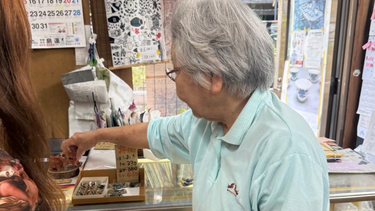 Dona Arakaki Kimie (新垣紀美江) tem oitenta anos e trabalha na sua loja há cinco décadas. Ela mostra com orgulho as peças artesanais aos vários turistas brasileiros do local. Foto: Adriana Barroli