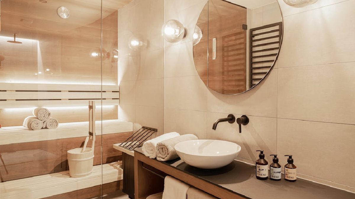 A presença de sauna e espelho amplo aproxima o banheiro da lógica de bem-estar dos hotéis, onde o banho também é pensado como experiência de permanência (Foto: Omaela Apartments / Pexels)