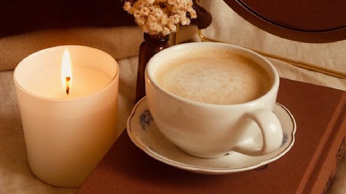 Café, vela e livro traduzem visualmente a atmosfera de hygge, palavra dinamarquesa usada para falar de aconchego e bem-estar em cenas íntimas do cotidiano (Foto: Esra Nur Kalay / Pexels)