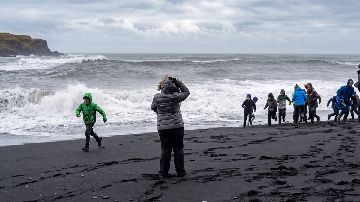 Visitantes caminham pela areia negra de Reynisfjara, considerada uma das praias mais bonitas e instáveis do mundo. Foto: Reprodução/Youtube